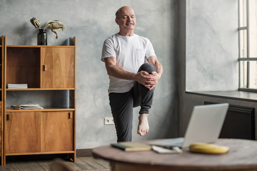 uomo anziano che fa yoga davanti al PC